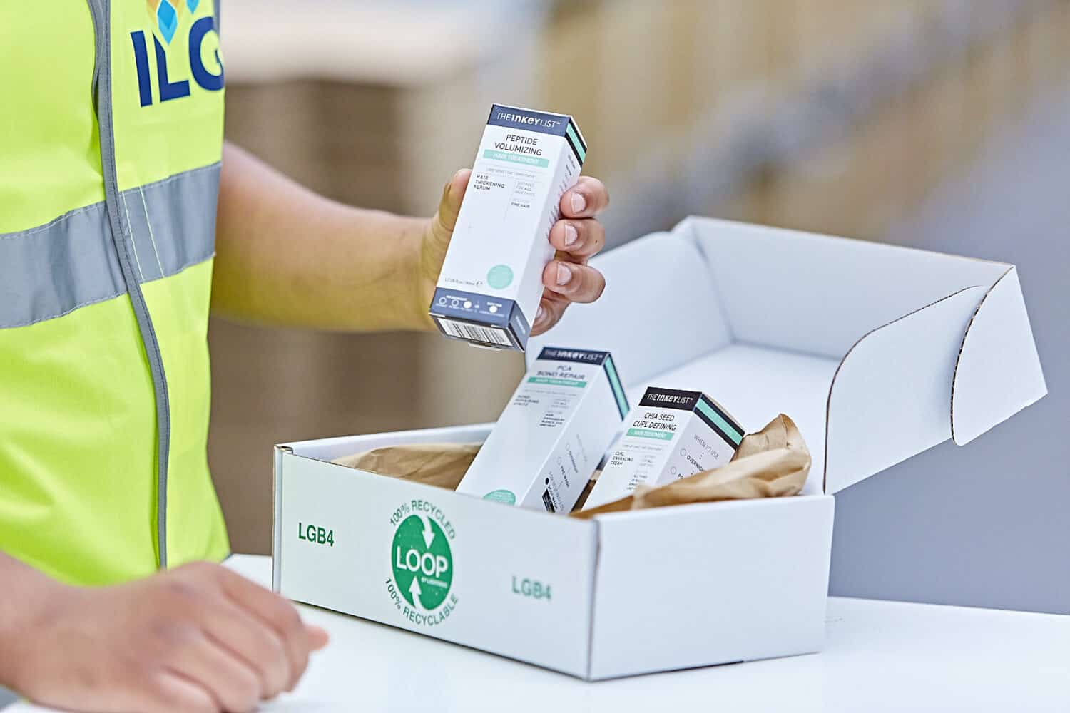 ILG warehouse employee in a high vis jacket packing a box of beauty products